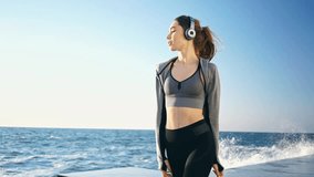 Side view of Smiling Pretty brunette sports woman in headphones walking at the seaside
