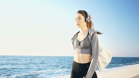 Side view of Pretty brunette sports woman in headphones walking at the seaside