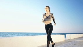 Full length view of Pretty brunette sports woman in headphones running at the seaside