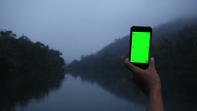 Hand using smartphone green screen at river