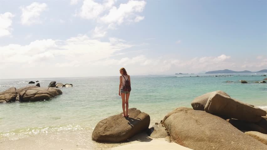 girl standing with her back on the rocks on the beach raising her hands