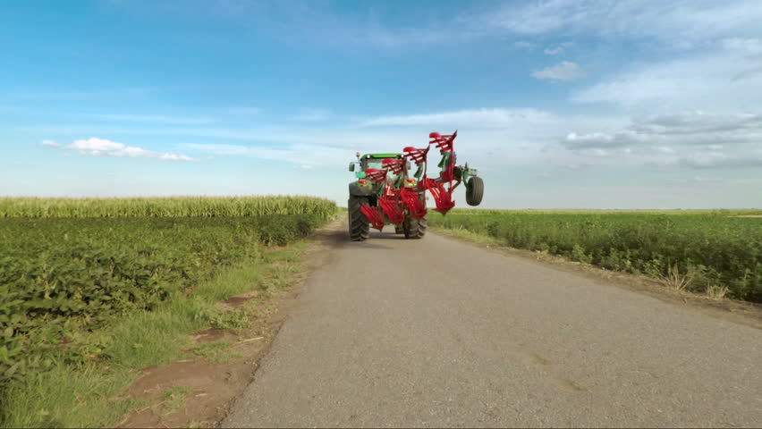 Rear view of tractor with a plow goes into the field.