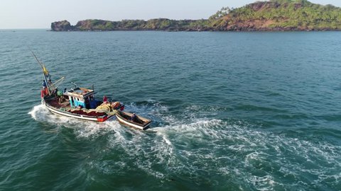 The old Indian fishing boat is rapidly moving dissecting waves along the shores of a beautiful bay. The camera flies 360 degrees at a low altitude. Aerial view.