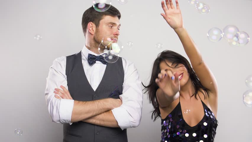 Party, fun and holidays concept - happy woman dancing in soap bubbles next to bored man