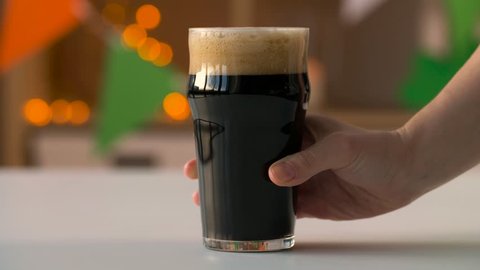 holidays, celebration and st patrick's day concept - female hand putting glass of dark draught beer on table