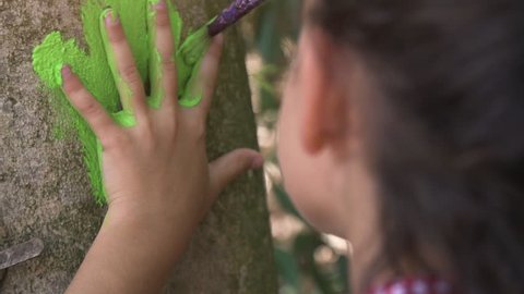 Happy young girl in summer camp leaving handprints with colorful paint on trees art outside kids playing outdoor in park under trees slow motion