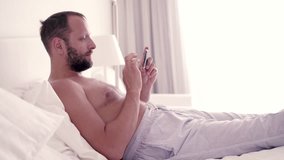 Happy man watching movie on smartphone lying on bed, 4K