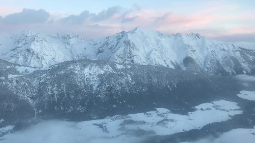 Winter mountains with snow and clouds filmed from airplane landing at Innsbruck during sunrise. Austria. Alps