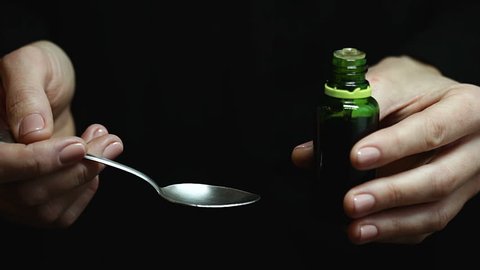 Woman drips liquid medicine out of green bottle into spoon. Few drops of syrup
