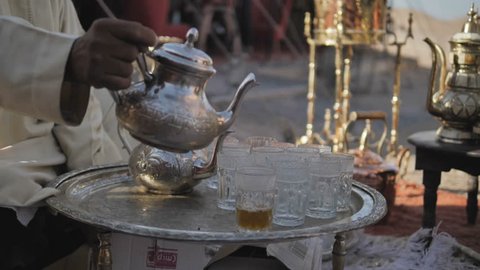 Morocco, Man pouring tea from ornate silver teapot into glasses on small table