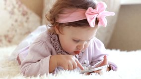 Funny child lying in bed downloads application on a smartphone. Portrait of a cute little girl closeup, whose eyes are lowered downwards looking in the screen cell phone and playing the game.