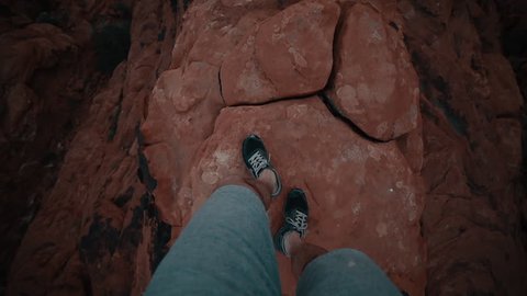 Looking Down at Feet Walking on Narrow Rocky Cliff above Canyon
