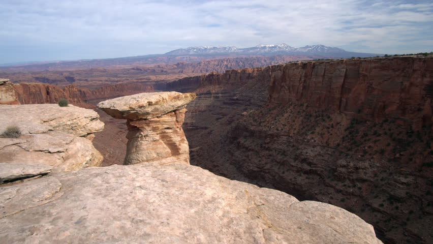 Walking along steep cliff edge viewing rock spire in Long Canyon near Moab Utah.