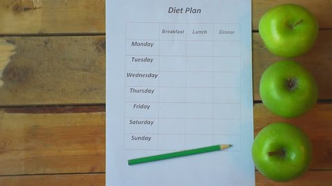 diet plan.ripe apple falls on a wooden table on which lies an empty food schedule. View from above