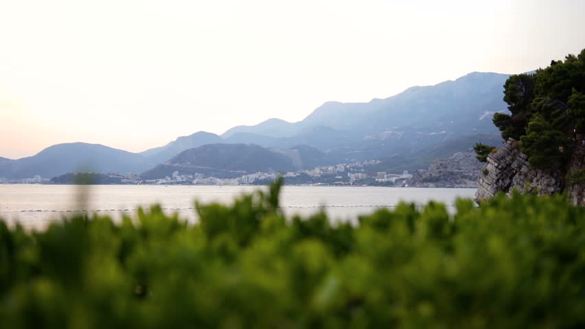 Beautiful landscape of the sea bay and shore with high mountains around it. Green blurred bushes in front. Outdoors