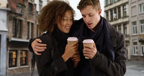 Cheerful young couple drinking coffee outdoors in Bruges. Millennial male and female tourists enjoy cup of coffee and sightsee on the streets. 4k