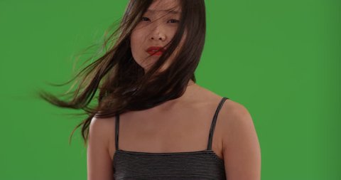 Close up of asian woman's face with hair blowing on green chroma key. Tight shot of young Chinese woman with long dark hair in the wind on greenscreen. 4k