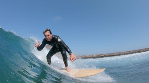 LOW ANGLE, UNDERWATER: Surfer gives the shaka sign before crashes into crystal clear blue ocean. Cool surfer dude jumping off surfboard into glassy water after successfully riding dangerous waves.