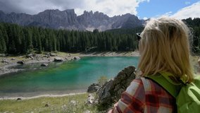 4K shot of a young woman making a heart shape finger frame on the beautiful alpine lake in Italy, Dolomites mountains o the background. Summer, travel people environment concept
