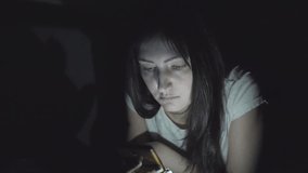 Young beautiful woman in the dark at night sits with a phone in social networks.
