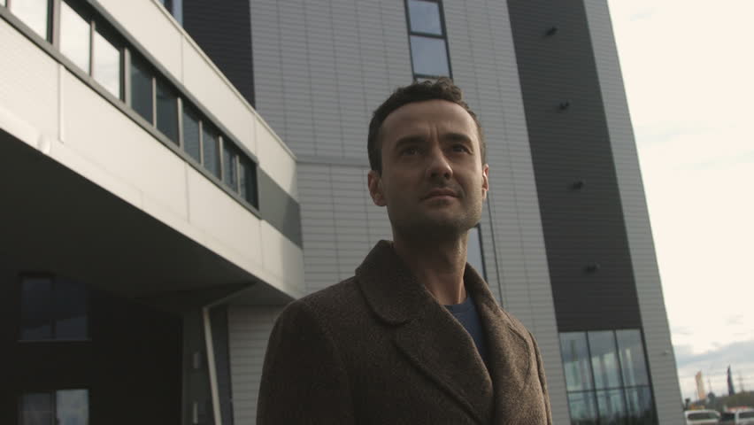 Urban portrait human in coat stand near contemporary office centre and watching forward. Businessperson keep calm and thinking. Successful concept new dynamic life in big town slow motion