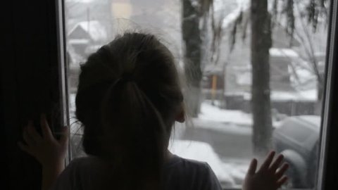 the child looks out the window at the snow