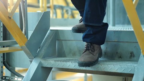 Close-up of worker's boots walking in heavy industry factory.