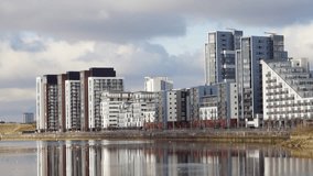 Panorama of modern  and stylish riverside flats with reflection in the water and flock of gulls circling in the middle distance.  Static shot.