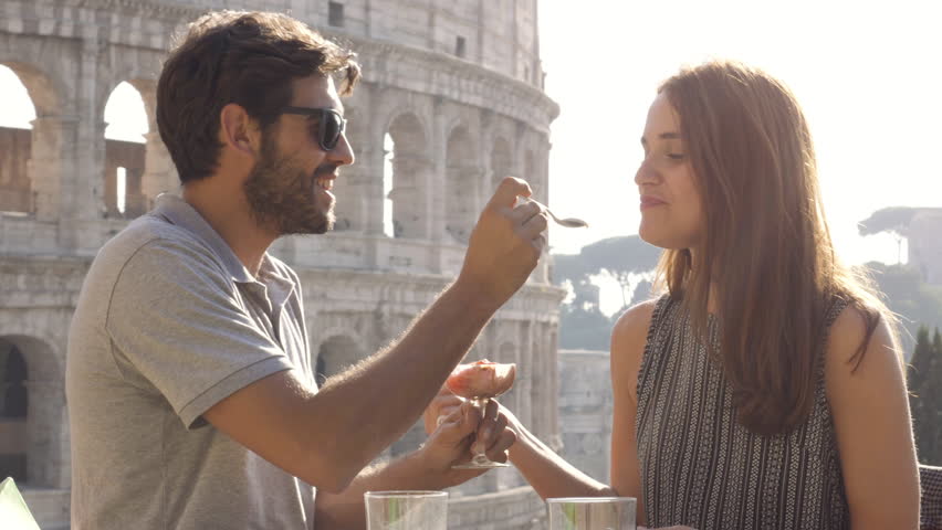 Happy young couple tourists eating glass of icecream sitting at bar restaurant outside in front of colosseum in rome at sunset Royalty-Free Stock Footage #1007358019