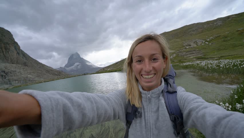 Young woman hiking in Switzerland takes selfie portrait by stunning alpine lake, Matterhorn in the background.
Hiker taking selfies on a hike in Zermatt, Switzerland 