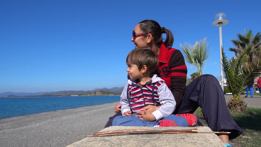 4K Mother and son wave with their hands to somebody in the sea
