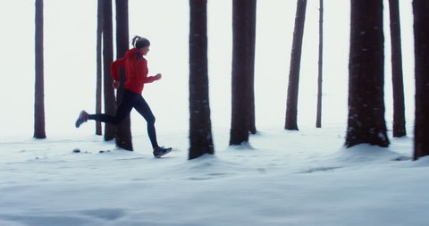 WIDE TRACKING SIDE VIEW Adult fit Caucasian female jogging on winter forest trail. 4K UHD 60 FPS SLO MO