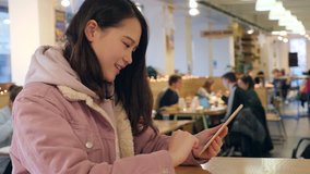 Chinese international student using smart phone in restaurant with different nationalities student in background.Shoot in Bristol, UK.