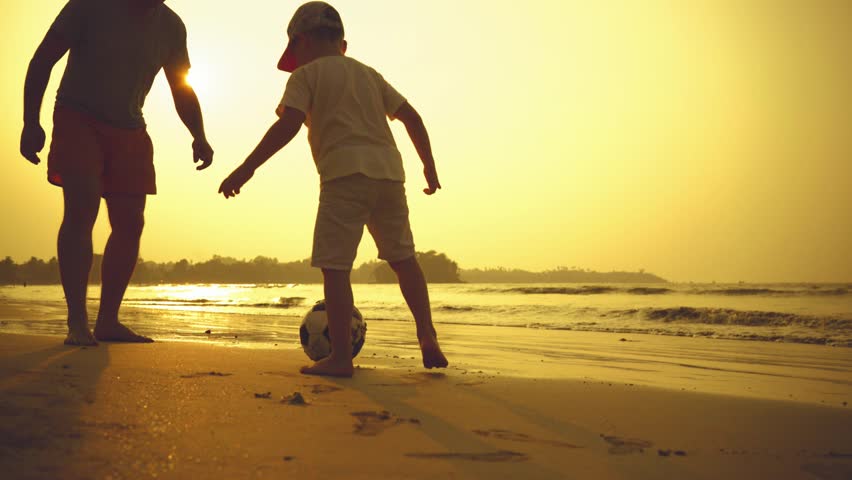 Father and son playing together with ball in football on the beach under sunset background | Shutterstock HD Video #1007368267