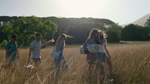 Group of friends holding blankets and food walking in field to have a pinic, roadtrip carefree summer freedom