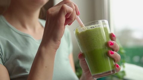 Woman is staying near window with glass of green smoothie
