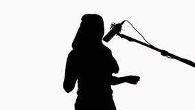 Silhouette of a girl with long hair who sings into a studio microphone. On a white background. Recording a music video