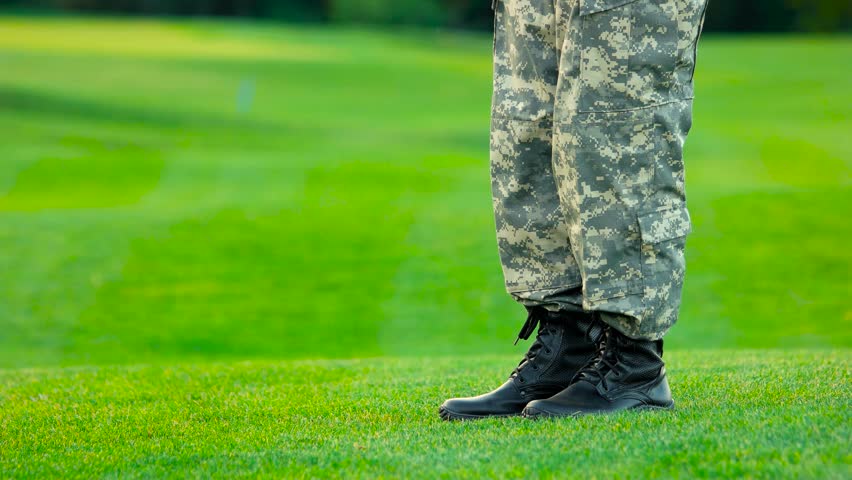 Woman stand on her toes to kiss her soldier boyfriend. Young military couple kissing each other, homecoming concept.