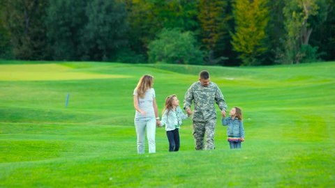 Happy soldier with his family in park. Man in camoubackgrounde, wife and two little daughters.