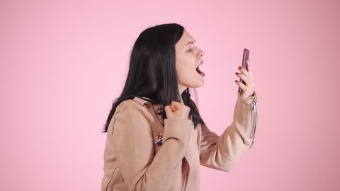Angry modern businesswoman screaming down her mobile phone in slow motion. Stressed and depressed girl on pink background.