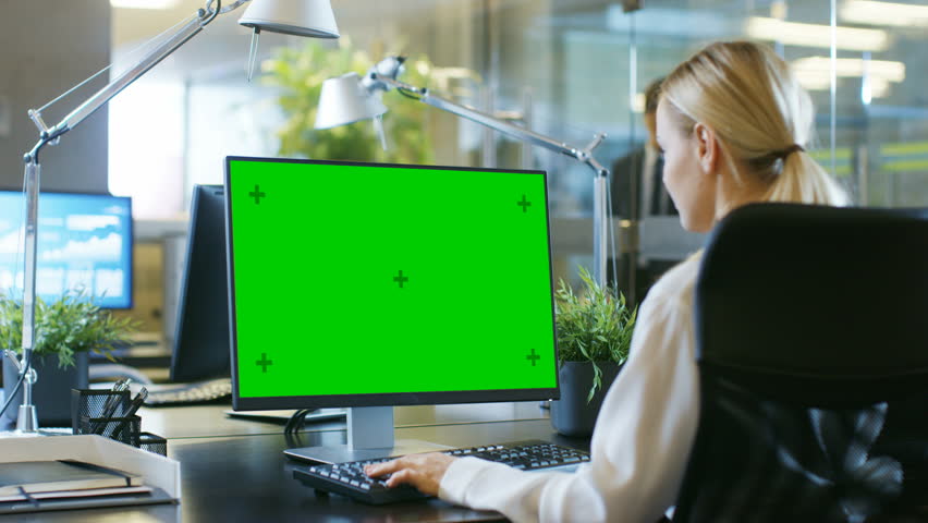 In the Office Businesswoman works at Her Desk on a Personal Computer with Mock-up Green Screen. Colleague Enters Office and Takes Place at His Desk.