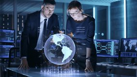 Male and Female Agents Futuristic Table With Futuristic Holographic 3D Interface. In the Monitoring Room of Special International Security Unit Tracking Targets. - Powered by Shutterstock - Get 15% off with code: PIKWIZARD15