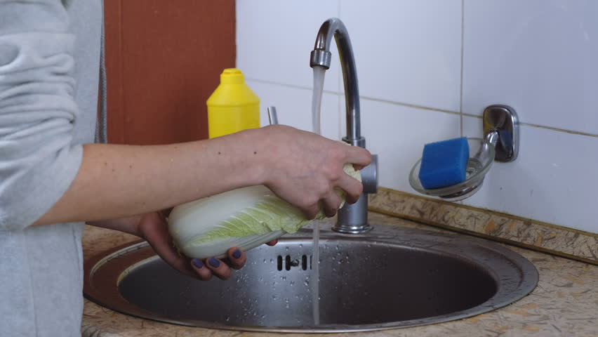Unrecognizable woman washes chinese cabbage in the kitchen. Side view.