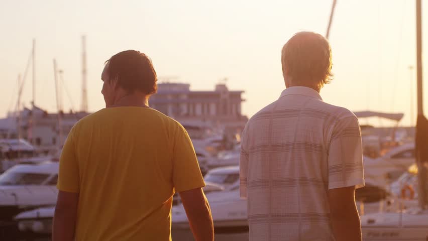 Two friends are walking at the promenade. Beautiful golden sunset at the yachts beach and lens flarre effect. slow motion. 1920x1080