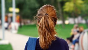 Back view of Young brunette woman walking with backpack in park