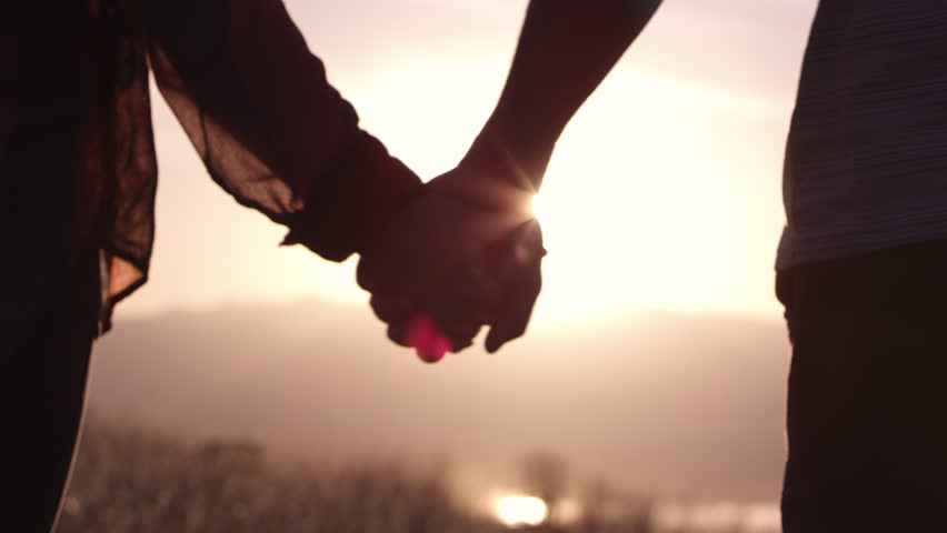 Couple holding hands walking out of focus towards sunset sun lens flare. Royalty-Free Stock Footage #1007418898
