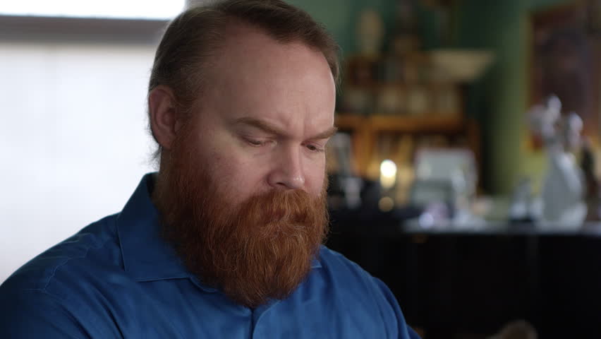Man with big red beard leaning his head on his hands as he is deep in thought.