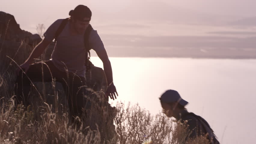 Young man helping others up steep mountain path as they reach for his hand he pulls them up the hill, slow motion. Royalty-Free Stock Footage #1007420158