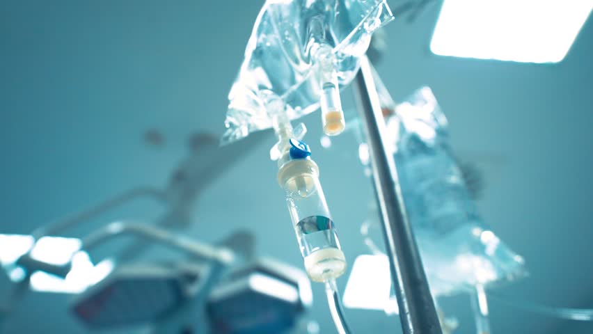 Intravenous drip in focus,surgeons team performing operation in the background,out of focus,infusion dripping.  Royalty-Free Stock Footage #1007427886