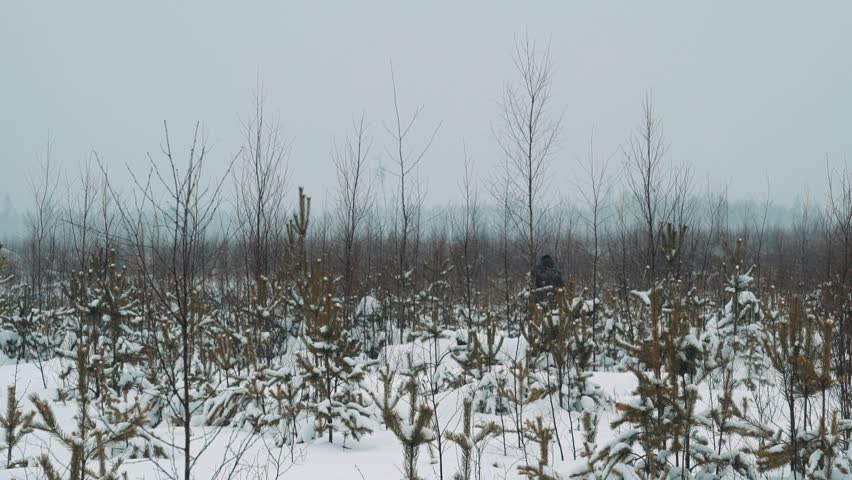 Young hiker in warm clothes and backpack walking on snow covered prairie shrubbery on cold cloudy winter day